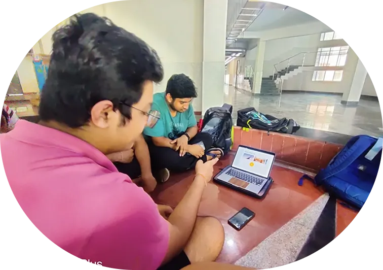 Two students huddled around a laptop at a college corridor, working on a product design project
